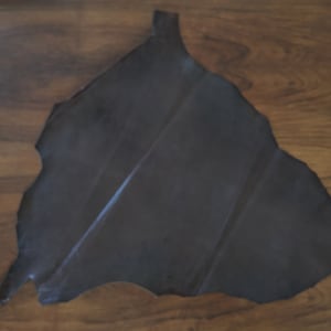 May include: A dark grey leather hide with a rough, irregular edge. The leather is smooth and appears to be supple.