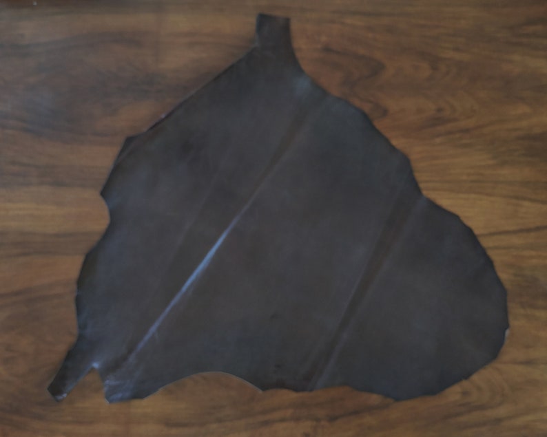 May include: A dark grey leather hide with a rough, irregular edge. The leather is smooth and appears to be supple.