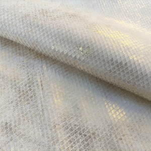 Può includere: Tessuto in pelle bianca con un leggero luccichio dorato. Il tessuto presenta un motivo testurizzato a forma di diamante.