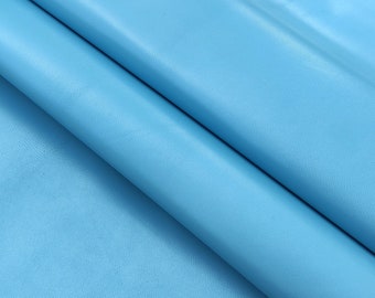 May include: A close-up of a smooth, light blue leather fabric. The fabric is folded in half, showing the texture and color.