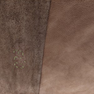 Pode incluir: Close-up de duas sec&ccedil;&otilde;es de couro. O lado esquerdo &eacute; castanho &aacute;spero e texturizado, com a palavra "E.G." costurada em verde. O lado direito &eacute; couro liso e castanho claro. A imagem mostra um contraste de texturas e cores.