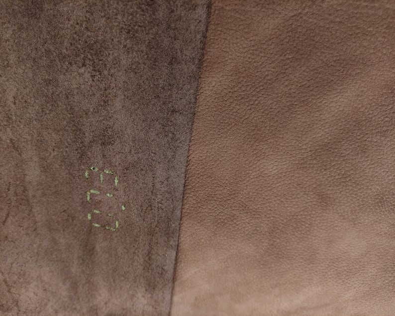 Pode incluir: Close-up de duas sec&ccedil;&otilde;es de couro. O lado esquerdo &eacute; castanho &aacute;spero e texturizado, com a palavra "E.G." costurada em verde. O lado direito &eacute; couro liso e castanho claro. A imagem mostra um contraste de texturas e cores.