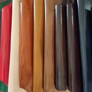 May include: A collection of leather samples in various colours, including green, red, beige, brown, orange, tan, dark brown, navy blue, and black. The leather is smooth and shiny, with a slight sheen.