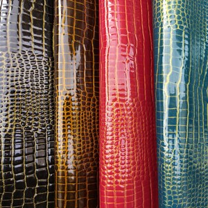 May include: Four rolls of faux leather with a crocodile skin pattern. The rolls are black, brown, red, and blue.