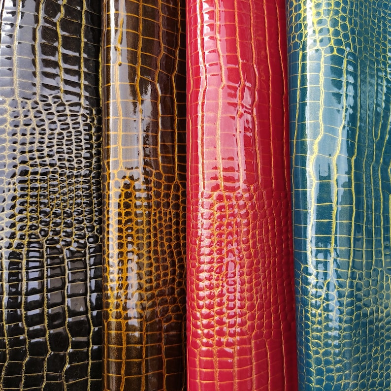 May include: Four rolls of faux leather with a crocodile skin pattern. The rolls are black, brown, red, and blue.