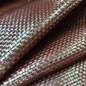 Puede incluir: Un material de color marrón oscuro con una textura tejida similar a una cesta y un acabado brillante. La superficie muestra un patrón de cuadrícula repetitivo de tiras entrelazadas, creando un aspecto dimensional con reflejos de luz.