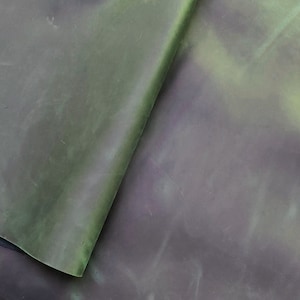 Puede incluir: Primer plano de un trozo de cuero verde con un efecto moteado y marmoleado. El cuero está doblado, revelando un lado inferior verde más oscuro.