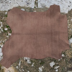 Pode incluir: Uma grande pe&ccedil;a de couro castanho de forma irregular. O couro tem uma textura macia, semelhante &agrave; camur&ccedil;a, e um acabamento mate. As bordas s&atilde;o irregulares, indicando um corte natural. O couro &eacute; provavelmente usado para a fabrica&ccedil;&atilde;o de artigos como bolsas ou estofados.