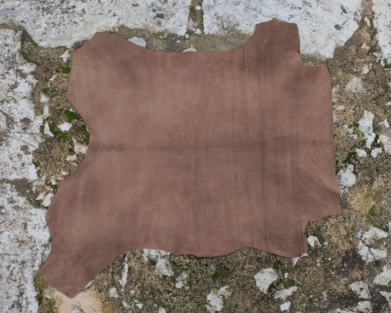 Pode incluir: Uma grande pe&ccedil;a de couro castanho de forma irregular. O couro tem uma textura macia, semelhante &agrave; camur&ccedil;a, e um acabamento mate. As bordas s&atilde;o irregulares, indicando um corte natural. O couro &eacute; provavelmente usado para a fabrica&ccedil;&atilde;o de artigos como bolsas ou estofados.