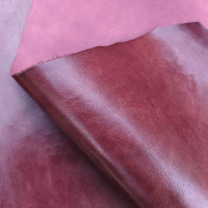 以下が含まれることがあります： 赤とピンクの色合いの革の2つの部分のクローズアップ。 上の部分は無地の明るいピンク色で、下の部分はわずかな光沢のある、より暗く、質感のある赤色です。 革の端はざらざらしていて未完成です。