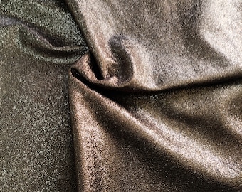 May include: Close-up of a metallic fabric with a shimmery, textured surface. The fabric is folded and draped, creating a soft, flowing effect.