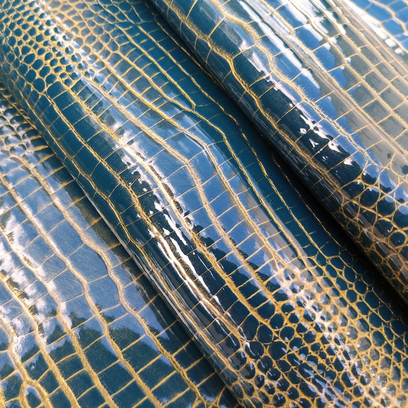 May include: Close-up of teal blue faux leather with a crocodile embossed pattern and a gold sheen.