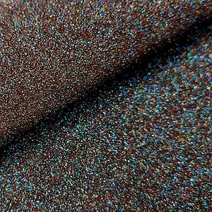 Puede incluir: Primer plano de una tela marrón oscura con purpurina iridiscente. La purpurina es una mezcla de azul, verde, dorado y rosa.