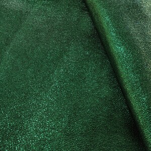 Puede incluir: Primer plano de una tela verde esmeralda con una superficie texturizada y brillante. El material tiene un brillo sutil, con pliegues que crean sombras y reflejos. La tela parece ser un textil lujoso, posiblemente para ropa o decoraci&oacute;n del hogar.