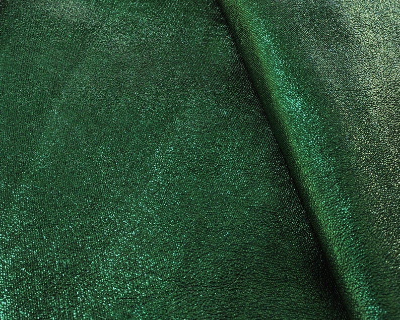 Puede incluir: Primer plano de una tela verde esmeralda con una superficie texturizada y brillante. El material tiene un brillo sutil, con pliegues que crean sombras y reflejos. La tela parece ser un textil lujoso, posiblemente para ropa o decoraci&oacute;n del hogar.