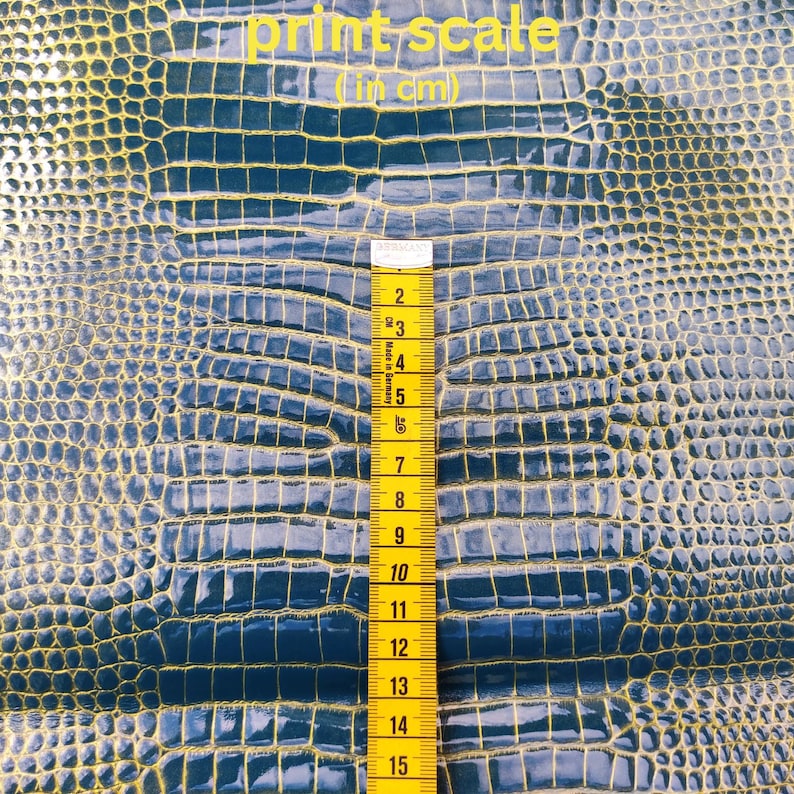 May include: A close-up of a blue textured fabric with a yellow scale pattern. A yellow measuring tape is placed vertically on the fabric, showing measurements in centimeters from 2 to 15.