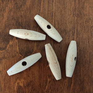 May include: Five wooden toggle buttons with a hole in the centre. The buttons are light brown and have a smooth finish.