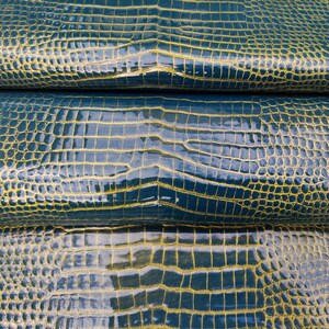May include: Close-up of a blue and yellow crocodile embossed leather. The leather has a glossy finish and a textured pattern.