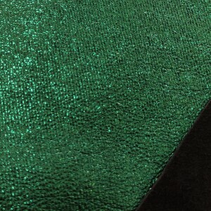 Puede incluir: Primer plano de una tela verde esmeralda texturizada con un aspecto brillante y moteado. Una secci&oacute;n diagonal de tela negra es visible en la esquina inferior derecha, creando un contraste de color y textura.