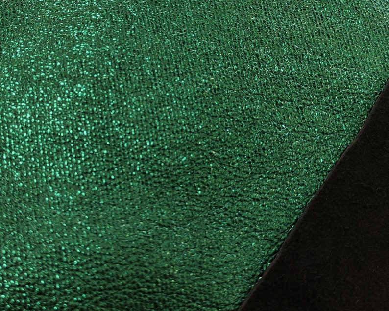 Puede incluir: Primer plano de una tela verde esmeralda texturizada con un aspecto brillante y moteado. Una secci&oacute;n diagonal de tela negra es visible en la esquina inferior derecha, creando un contraste de color y textura.