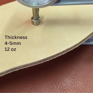 May include: Close-up of a piece of light tan leather being measured with a caliper. The text on the leather reads "Thickness 4-5mm 12 oz."