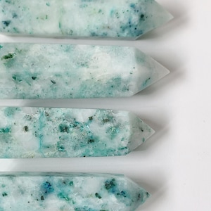 Könnte beinhalten: Vier weiße Kristallspitzen mit grünen und blauen Einschlüssen. Die Spitzen sind vertikal angeordnet, wobei die größte Spitze oben und die kleinste Spitze unten ist.