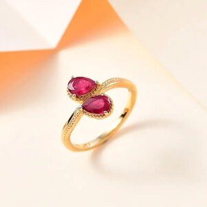 Puede incluir: Un anillo de oro con dos gemas rojas en forma de pera. La banda del anillo tiene un diseño texturizado y delicado. Las gemas están engastadas en un bisel de oro. Una elegante pieza de joyería.
