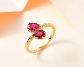 May include: A gold ring featuring two pear-shaped, deep red gemstones. The ring's band has a delicate, textured design. The gemstones are set in a gold bezel, creating a striking contrast. This elegant ring is a piece of fine jewelry.