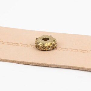 May include: A gold-colored metal stamp with a star-shaped design. The stamp is used to create decorative patterns on leather.
