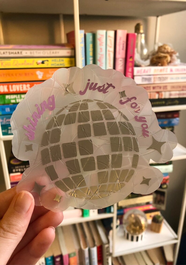 May include: A clear sticker with a disco ball design. The sticker has a scalloped edge and features the words "shining just for you" in pink script. Gold star accents surround the disco ball.