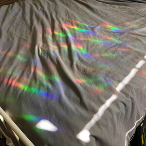 May include: A gray bedsheet is illuminated by a spectrum of rainbow-colored light, creating a vibrant display of colors. The light appears to be refracted, casting bands of red, orange, yellow, green, blue, and purple across the fabric.