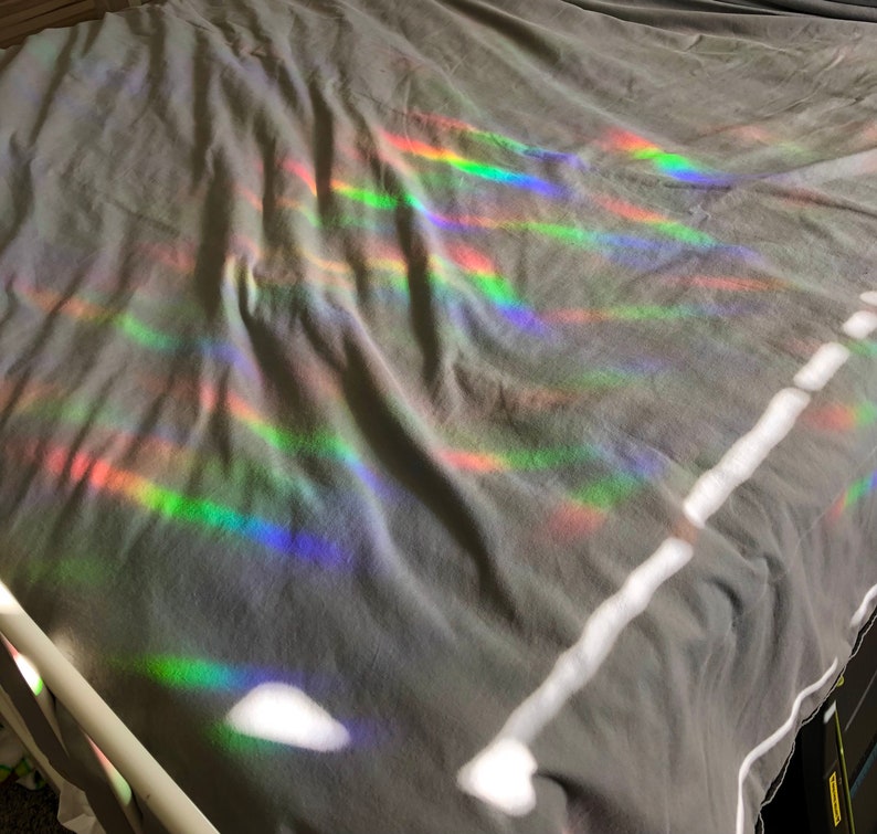 May include: A gray bedsheet is illuminated by a spectrum of rainbow-colored light, creating a vibrant display of colors. The light appears to be refracted, casting bands of red, orange, yellow, green, blue, and purple across the fabric.