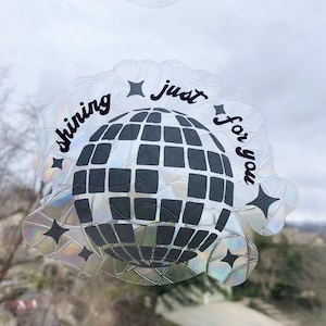 May include: A clear, iridescent sticker with a disco ball design and the words "shining just for you" in black script. The sticker has a scalloped edge and star accents. Two cloud-shaped stickers with smiley faces are visible above.