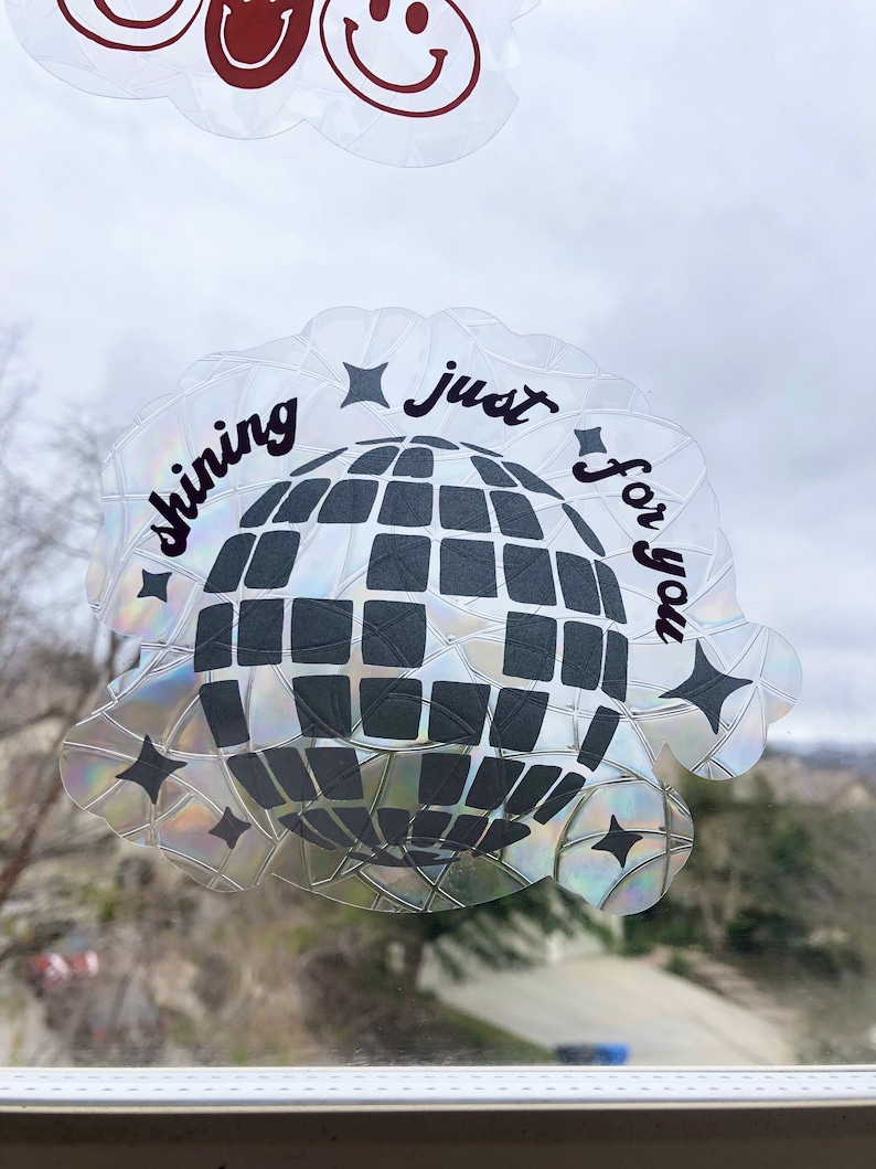 May include: A clear, iridescent sticker with a disco ball design and the words "shining just for you" in black script. The sticker has a scalloped edge and star accents. Two cloud-shaped stickers with smiley faces are visible above.