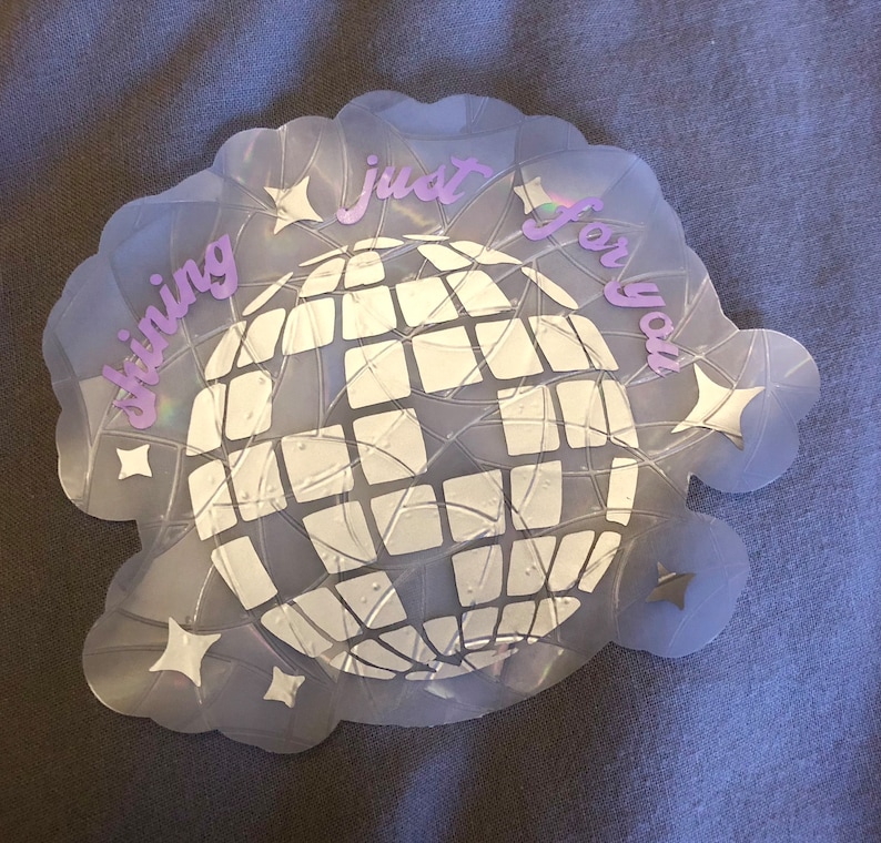 May include: A holographic sticker with a disco ball design. The sticker has the words "shining just for you" in a light purple script. The disco ball is white and surrounded by star shapes.