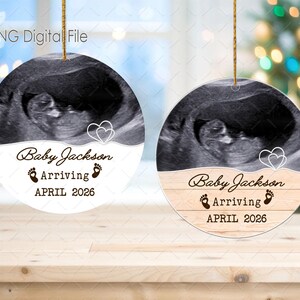 May include: Two circular ornaments featuring ultrasound scans. Each has the text "Baby Jackson Arriving APRIL 2026" with footprints and heart graphics. One has a wood effect design on the lower half.