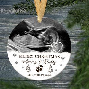 May include: A round Christmas ornament with a sonogram image. The ornament has a gold ribbon for hanging and features the text "MERRY CHRISTMAS Mommy & Daddy SEE YOU IN 2026" with snowflakes, footprints, and Christmas trees.