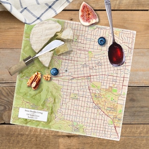 May include: A square cutting board with a map of Boulder, Colorado. The board is decorated with a variety of food items, including cheese, nuts, blueberries, and a fig. The text "Sweet Boulder Living" and "320 Spruce Street, Boulder, CO" is printed on the board.