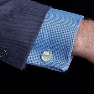 May include: A pair of cufflinks featuring a map of an island. The cufflinks are silver and have a blue and yellow map design.