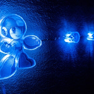 Könnte beinhalten: Eine blaue Lichterkette mit einer Comic-Roboterfigur. Die Lichter sind mit einem schwarzen Kabel verbunden.