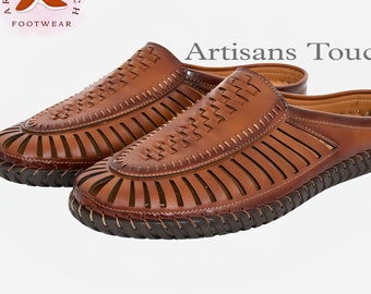 May include: A pair of brown leather sandals with a woven design and an open toe. The sandals have a brown leather strap across the top of the foot and a brown leather strap around the ankle. The sandals are made by Artisans Touch Footwear.