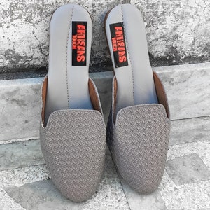 May include: A pair of gray leather slip-on shoes with a woven pattern. The shoes have a black label that says "Artisans Touch" on each shoe.