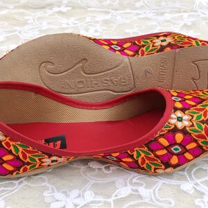 May include: A pair of red flat shoes with a floral embroidered design. The shoes have a brown sole and the text "FASHION" is printed on the sole.