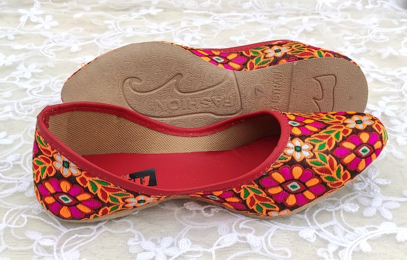 May include: A pair of red flat shoes with a floral embroidered design. The shoes have a brown sole and the text "FASHION" is printed on the sole.