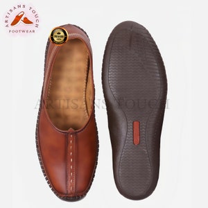 May include: A pair of brown leather slip-on shoes, one showing the top and the other the sole. The top shoe has white stitching and a decorative seam. The sole is dark brown with a textured pattern. The logo "ARTISANS TOUCH FOOTWEAR" is visible.