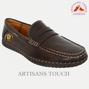 May include: Brown leather loafers with a stitched edge and a decorative stitching detail on the top. The loafers have a  "Premium Quality" label on the side. The text "Artisans Touch Footwear" is visible at the top of the image.