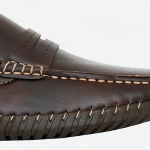 May include: Brown leather loafers with a stitched seam around the edge of the sole. The loafers have a slip-on design and a decorative stitch detail on the top.
