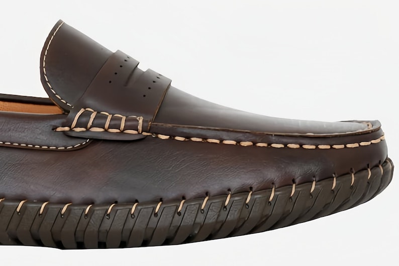 May include: Brown leather loafers with a stitched seam around the edge of the sole. The loafers have a slip-on design and a decorative stitch detail on the top.