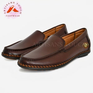 May include: A pair of brown leather loafers with a stitched edge and a brown leather sole. The loafers have a slip-on design and a rounded toe.