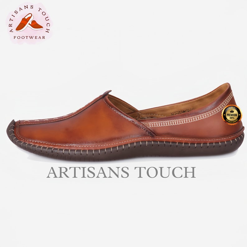 May include: A brown leather slip-on shoe with a square toe and stitched detailing. The shoe has a dark brown sole and a light brown interior. The words "ARTISANS TOUCH" are printed at the bottom of the image.